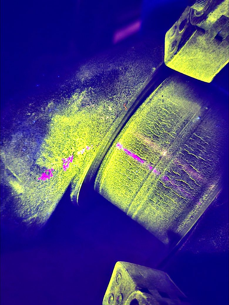 Fluorescent magnetic particle indications glowing under ultraviolet light on a TechRay NDT job